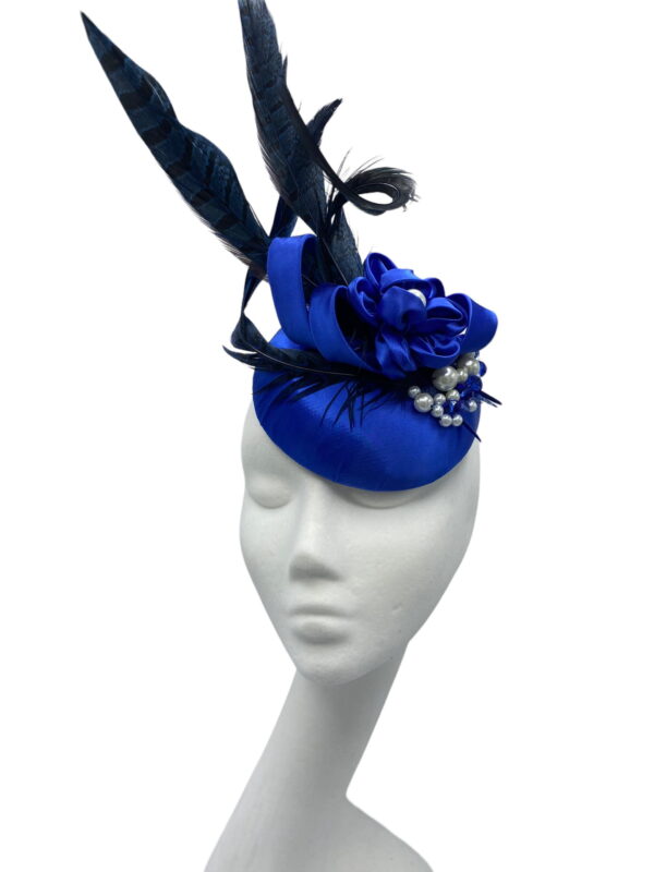 Small blue satin button headpiece with feather, swirl and pearl detail.